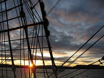 日落在borad 船上启航帆船波浪蓝色太阳绳索水手们血管天空水手背景图片