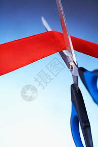 剪切红色丝带剪刀的特写图像商业庆典典礼仪式就职活动成就蓝色倾斜丝带背景图片