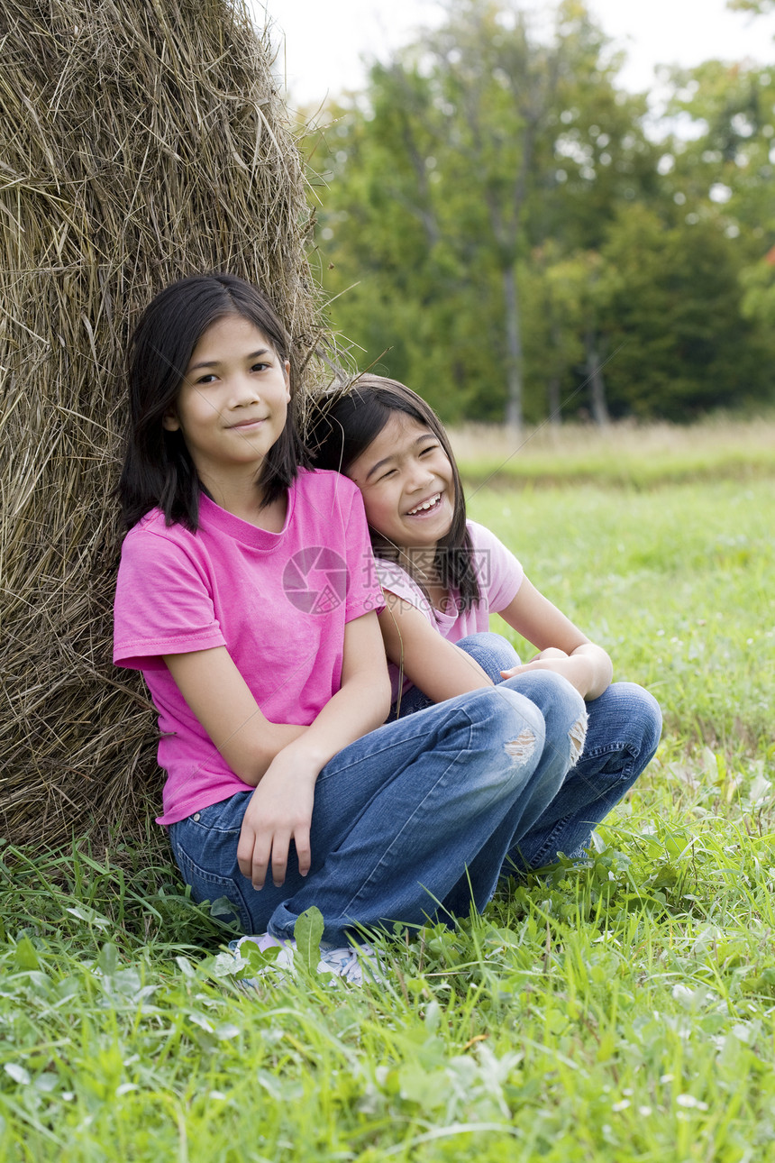 两个年轻女孩坐在对着干草树的旁边图片