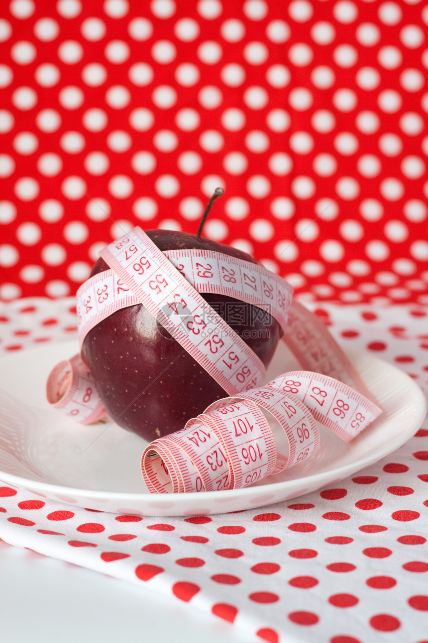 红苹果和在红色背景的白色盘子上的测量磁带活力重量饮食食物损失营养师乐队减肥水果图片