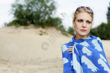 海滩上一个年轻美丽的女孩的肖像 她心烦意乱围巾耳环金发女郎蓝色肩膀眼镜女士背景图片