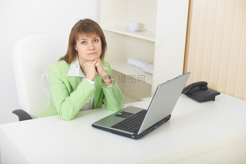 拥有膝上型电脑的年轻妇女坐在轻型办公室的桌子上家具老板商务悲伤人士戏服首席衣领扶手职场图片