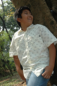 小男孩站在树旁边的树上公园白色孩子们蓝色青年衬衫孩子数字男性牛仔裤背景图片