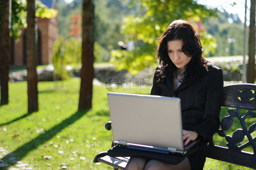 在公园里拿着笔记本的年轻女士头发电脑花园黑发自由互联网上网商业晴天技术图片