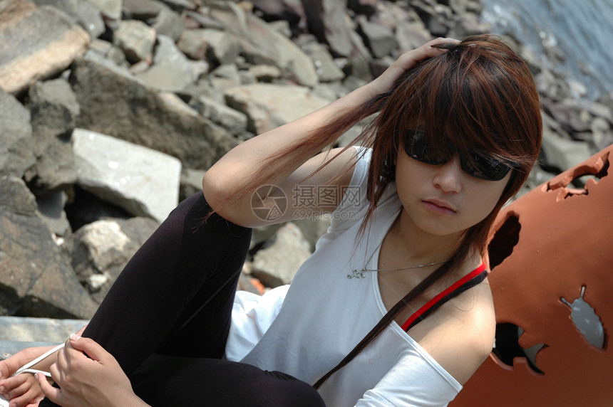 戴墨镜的年轻女士黑色头发牛仔裤数字假期身体青少年衬衫海滩岩石图片