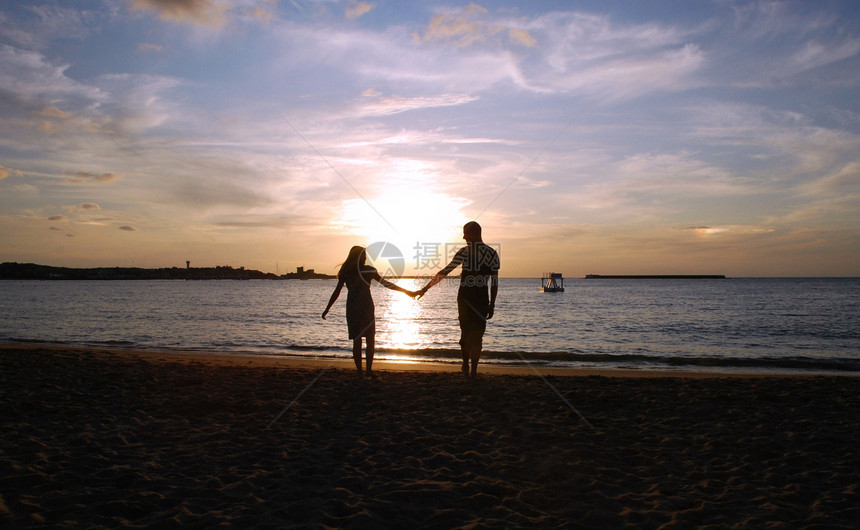 日落时的一对夫妇粉色海洋阴影海滩蓝色天空图片