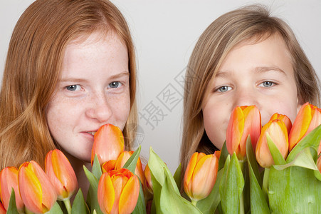 两个年轻女孩拿着粉红色橙色郁金香背景图片
