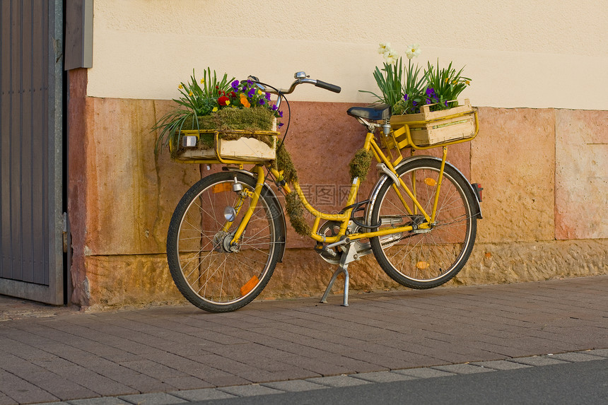 黄色自行车上的花朵植物石头木头绿色街道路面房子图片