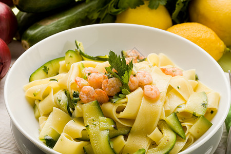 夏日食面与Zucchini和Shrimps的面食树叶叶子动物香菜甲壳类餐巾胡椒食物柠檬木桌背景