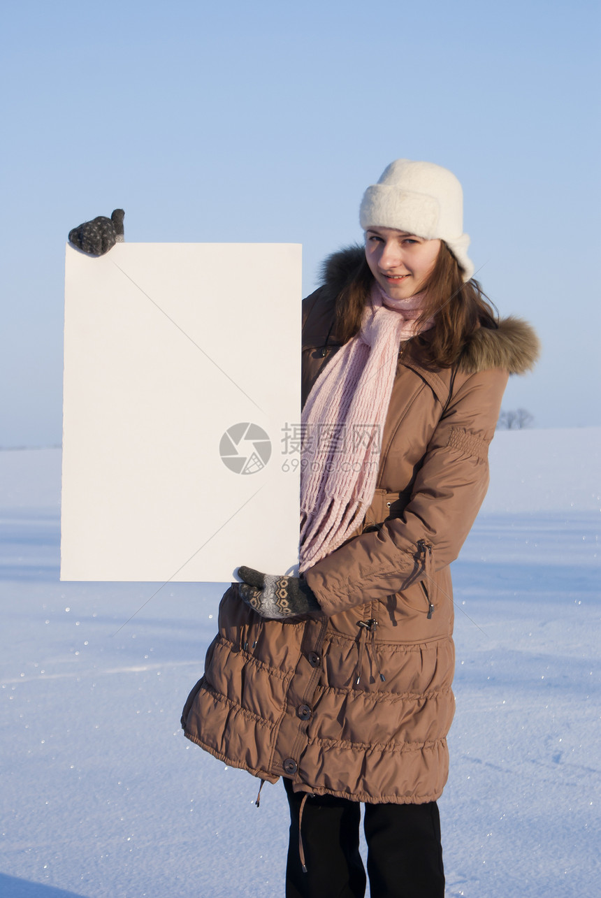 女孩在冬季雪田时张贴白海报标语微笑女性童年蓝色快乐公告孩子商业纸板图片