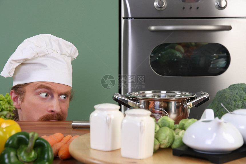 有趣的年轻厨师 奇怪地看着锅餐具白色男人衣服餐厅乐趣蔬菜帽子午餐烹饪图片