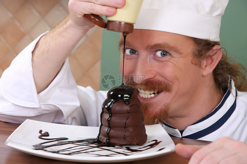有趣的年轻厨师 在一块蛋糕上加了巧克力酱汁糖果奶油职业乐趣甜点餐厅厨房衣服盘子男人图片