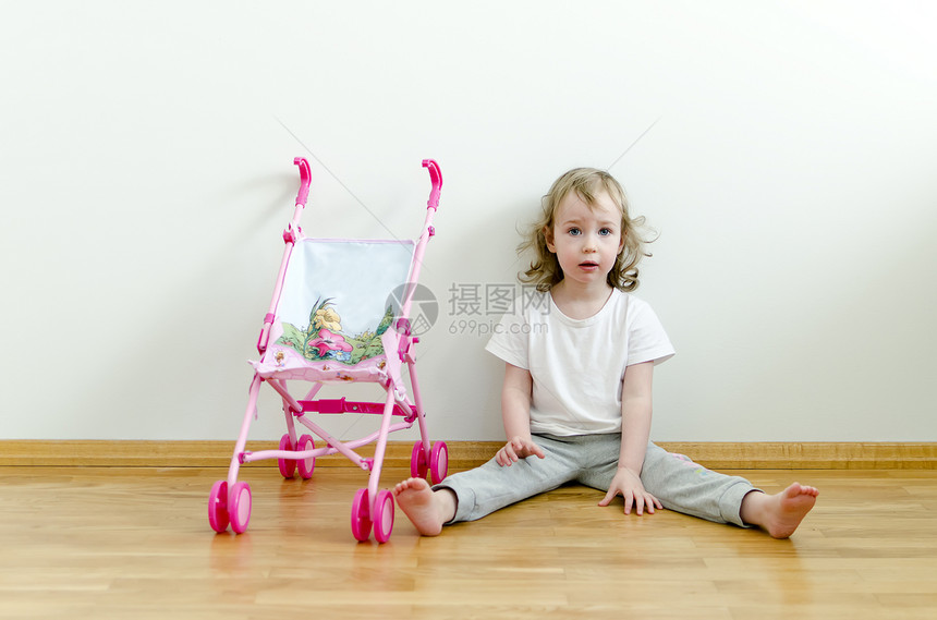 坐在玩具婴儿车旁边的地板上可爱的小可爱女孩图片