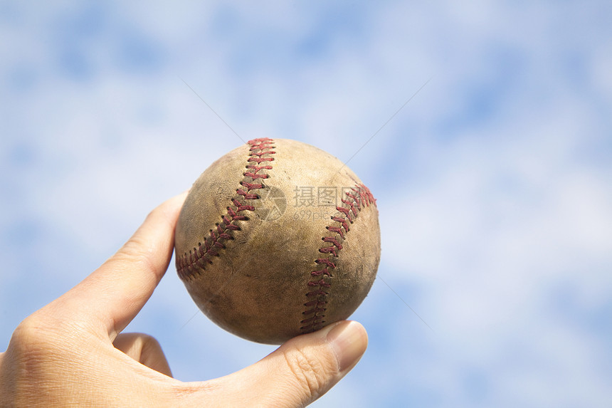 手握旧棒球和云幕背景图片