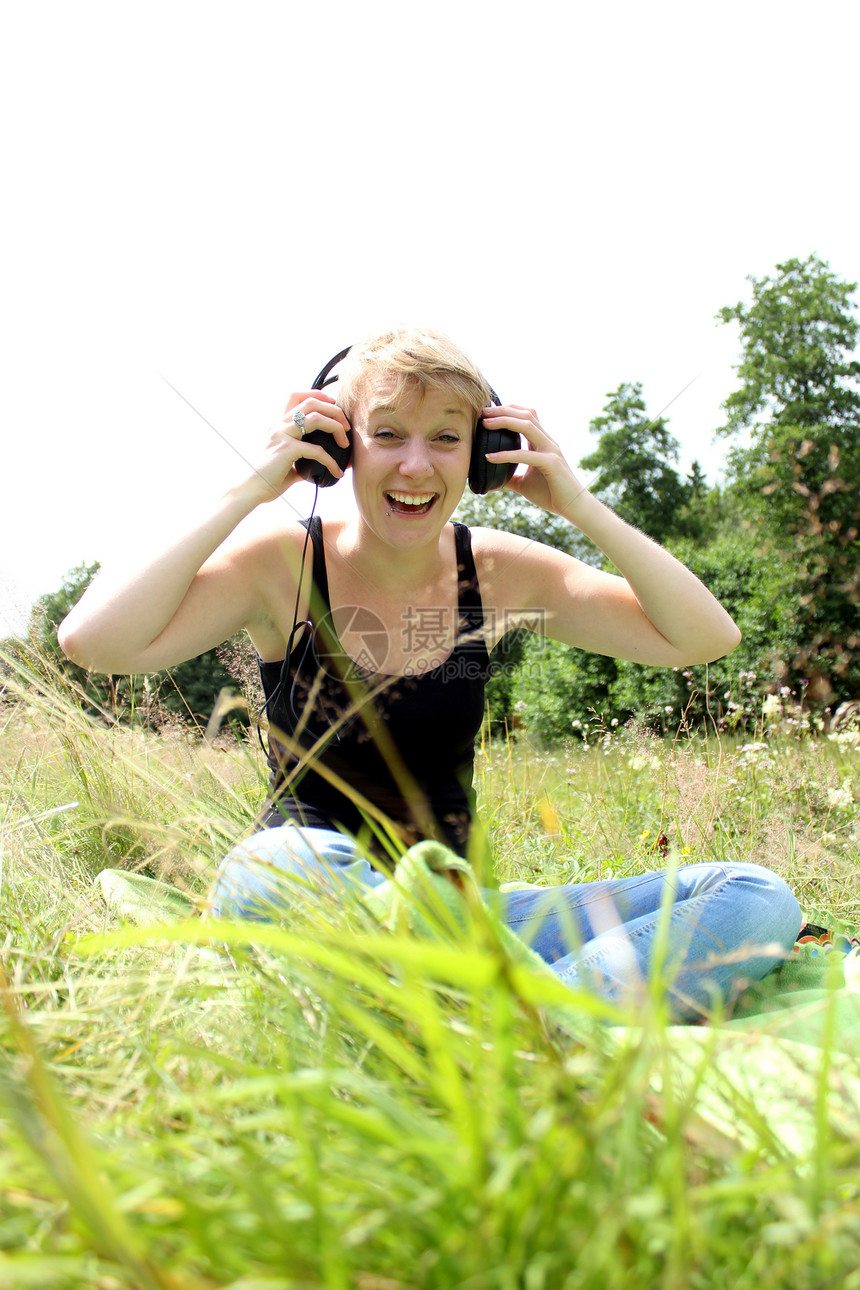 女孩用耳机在草地上女士学生自由幸福绿色喜悦娱乐公园女性音乐播放器图片