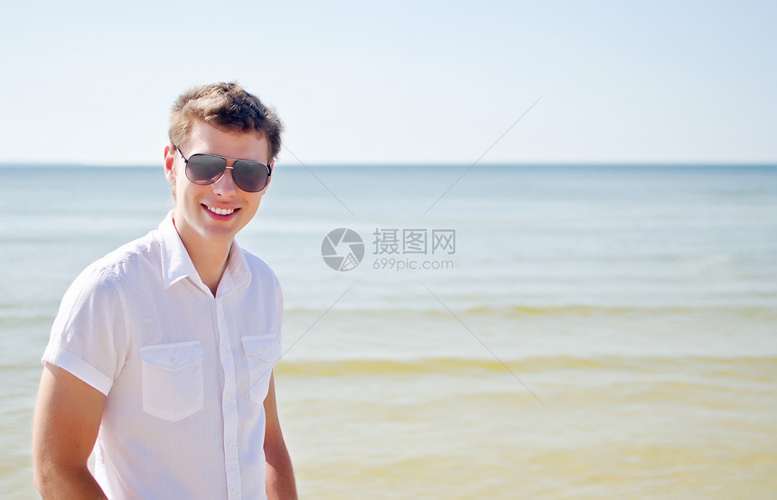 帅帅的笑脸家伙在海滩上 海在背景中天空冒充晴天闲暇海洋男人微笑支撑快乐享受图片