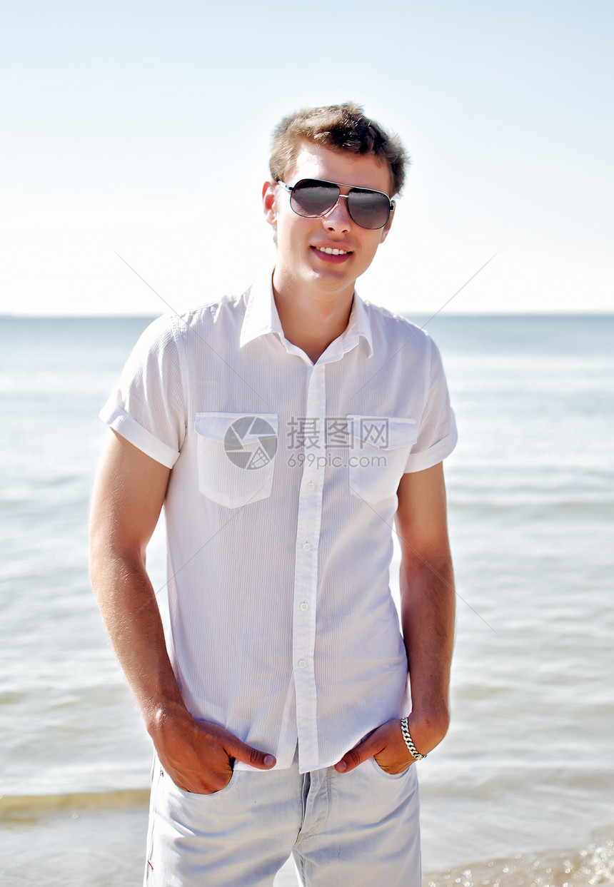 帅帅的笑脸家伙在海滩上 海在背景中男性闲暇旅行冒充支撑假期热带太阳镜晴天微笑图片
