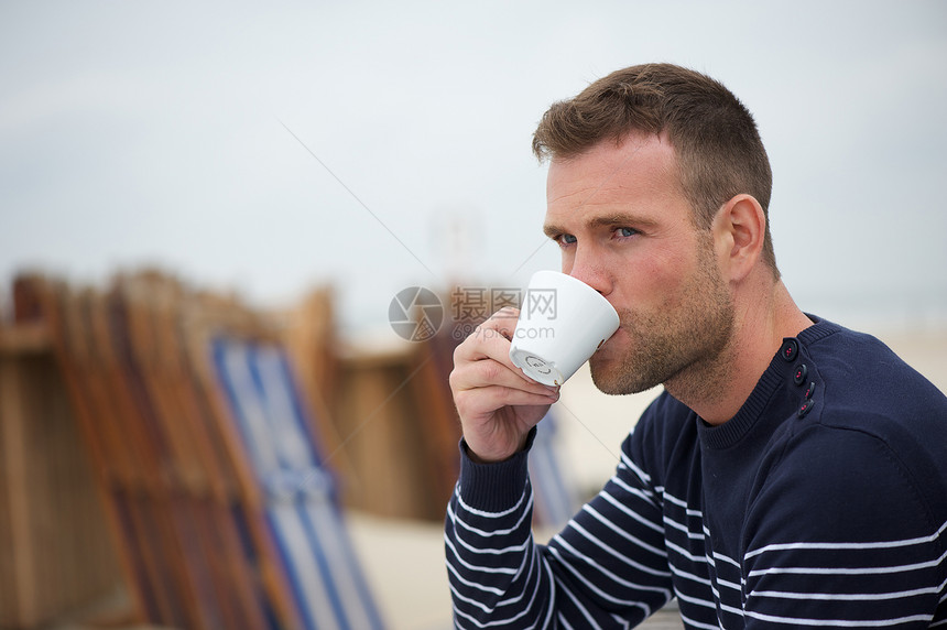 年轻人在沙滩喝咖啡毛衣饮料香气杯子椅子海洋男人咖啡海岸早餐图片