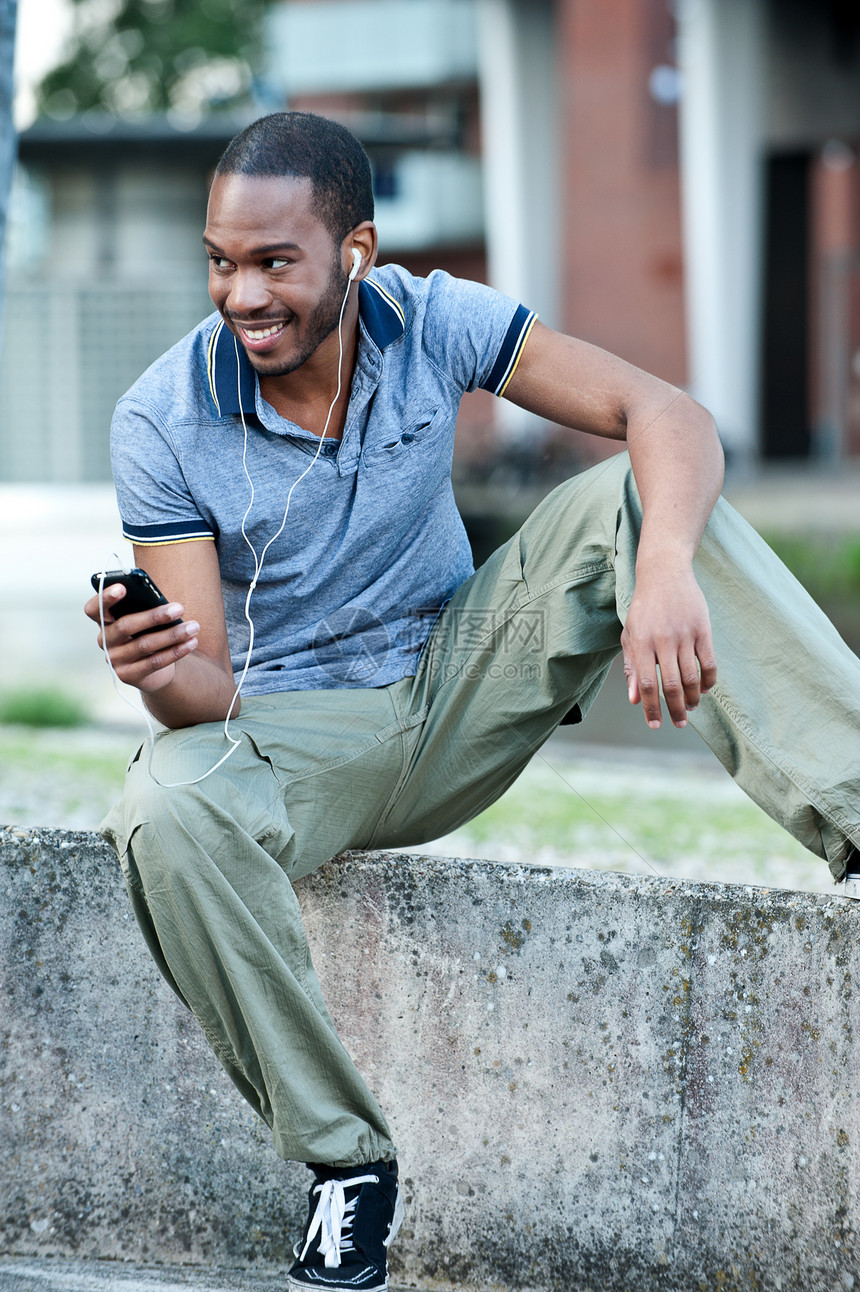 一位年轻黑人男性向外观望和听音乐的年轻人在外面耳机旁听音乐图片
