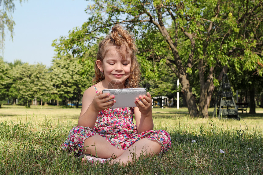 小女孩坐在公园里玩平板电脑Pc图片