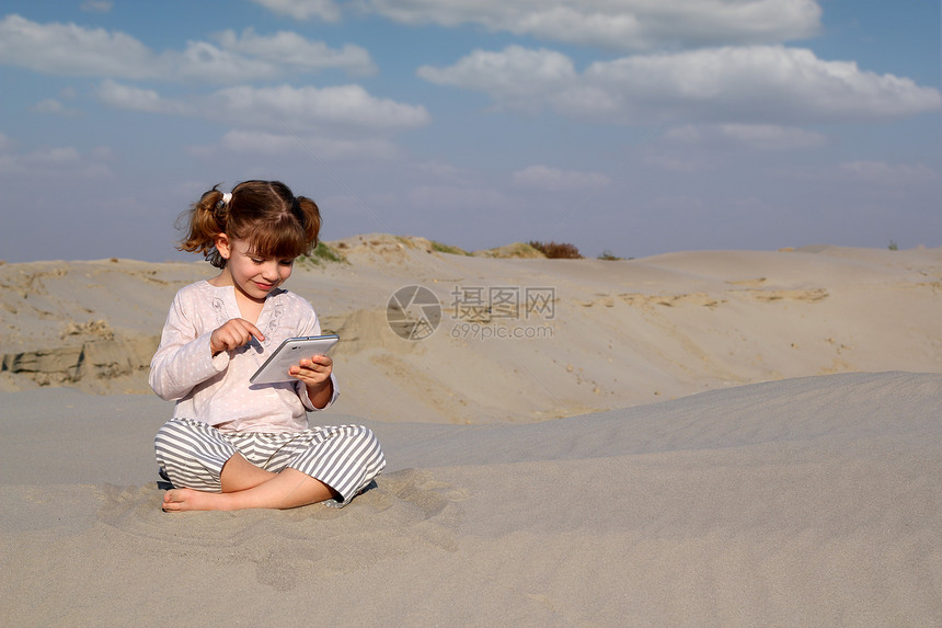 快乐的小女孩在沙漠玩平板电脑图片