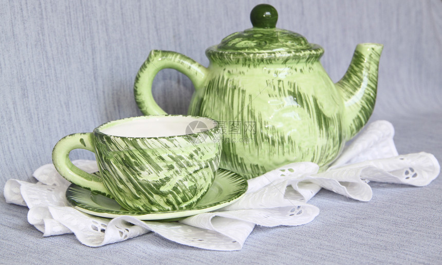 绿色茶壶和白花边餐巾纸上的杯子图片