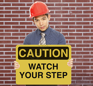当心跌倒标志注意脚步标志安全帽黄色施工安全砖墙指示牌建造业警告手表背景