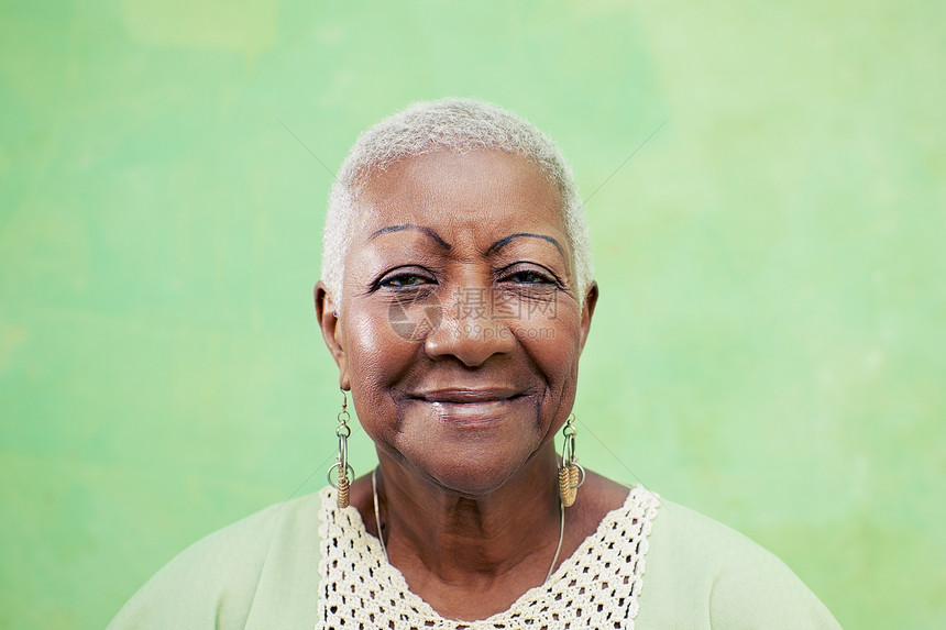高级黑人女性的肖像 在绿色背面对着镜头微笑黑色老年人快乐相机幸福老年祖母女士退休耳环图片