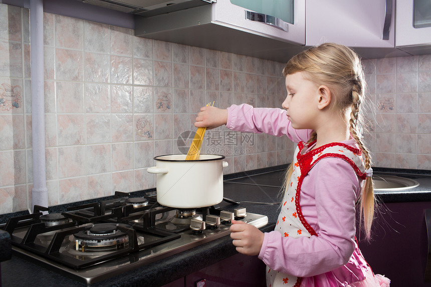 小女孩把意面放在锅里烹饪微笑孩子家庭女士女儿女孩紫色童年围裙图片