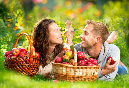 一对夫妇在秋园的草和吃苹果上放松女士篮子食物乐趣男生收成女孩采摘家庭果园背景图片