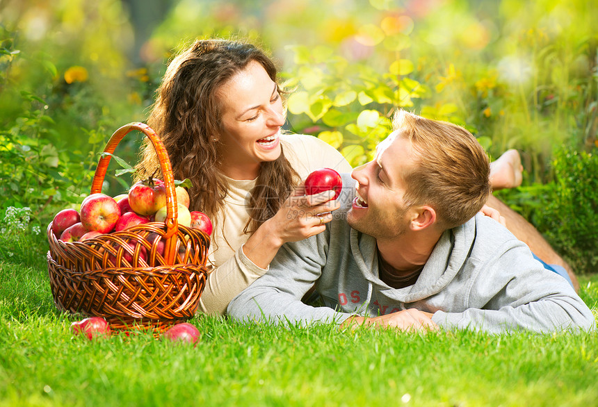 一对夫妇在秋园的草和吃苹果上放松收成家庭水果园艺牙科篮子太阳食物男生女士图片