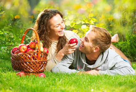 一对夫妇在秋园的草和吃苹果上放松收成家庭水果园艺牙科篮子太阳食物男生女士背景图片