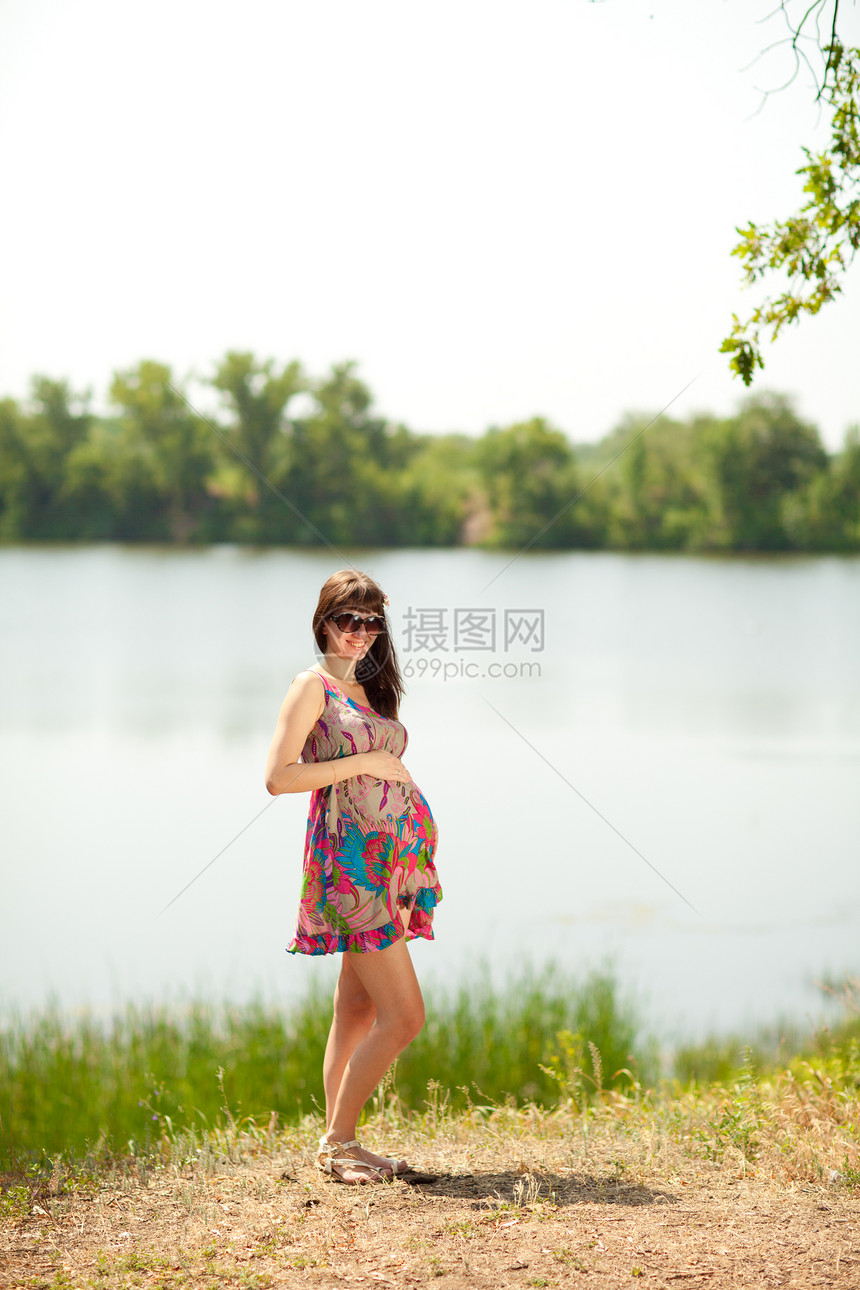 靠近湖边的怀孕女孩婴儿闲暇保健树木腹部海滩太阳镜母性幸福母亲图片