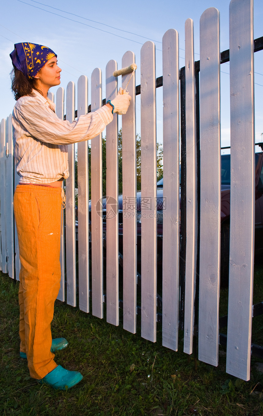 美丽的女孩在日落时给木栅栏着色住宅滚筒平反画家勤勉绘画康复装修栏杆女士图片