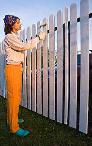 美丽的女孩在日落时给木栅栏着色住宅滚筒平反画家勤勉绘画康复装修栏杆女士背景图片
