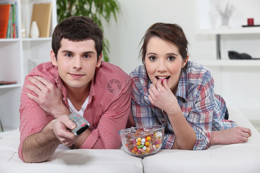 年轻夫妇用遥控器看电视 还有一碗甜食图片