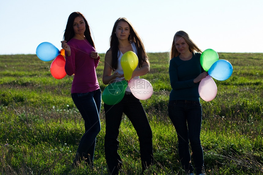 三名美丽的年轻女子 带着气球进入田野对抗自由头发团队幸福天空草地女性场景青少年喜悦图片