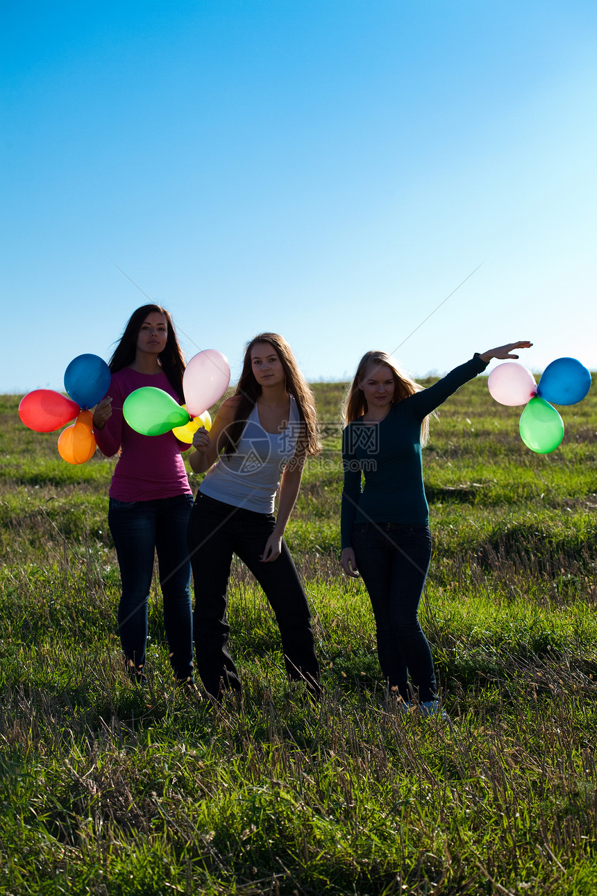 三名美丽的年轻女子 带着气球进入田野对抗女性阳光微笑假期草地友谊头发闲暇乐趣场景图片