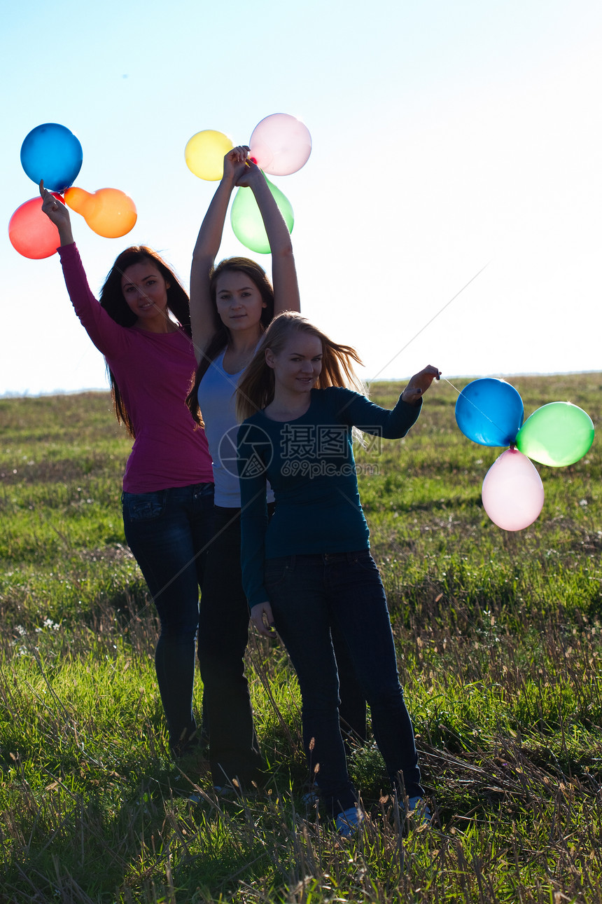 三名美丽的年轻女子 带着气球进入田野对抗草地幸福团体友谊太阳自由喜悦微笑阳光闲暇图片