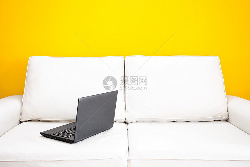 白沙发和笔记本电脑对着公寓的黄色墙壁图片