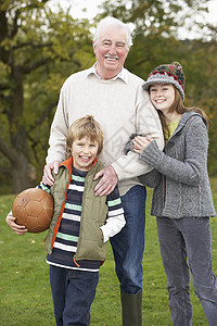 玩足球老人外祖父和孙子女在外持有橄榄球背景