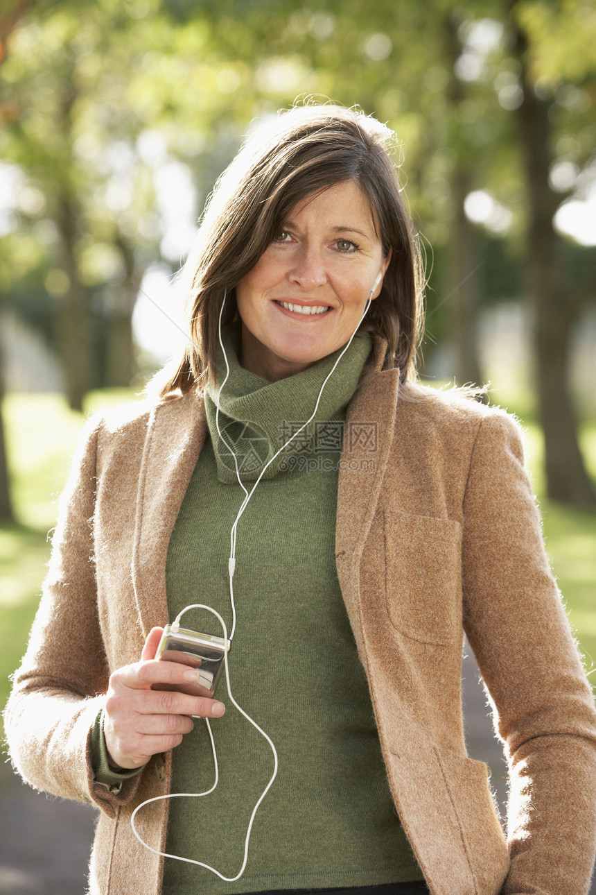女性在秋季公园散步时聆听MP3的音乐中年耳机黑发图片