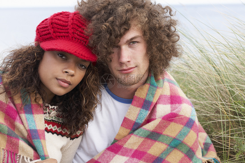 坐在沙洞中的年轻夫妇坐落在毯子中海滨亲热海滩长发男人衣服水平男性女性思维图片