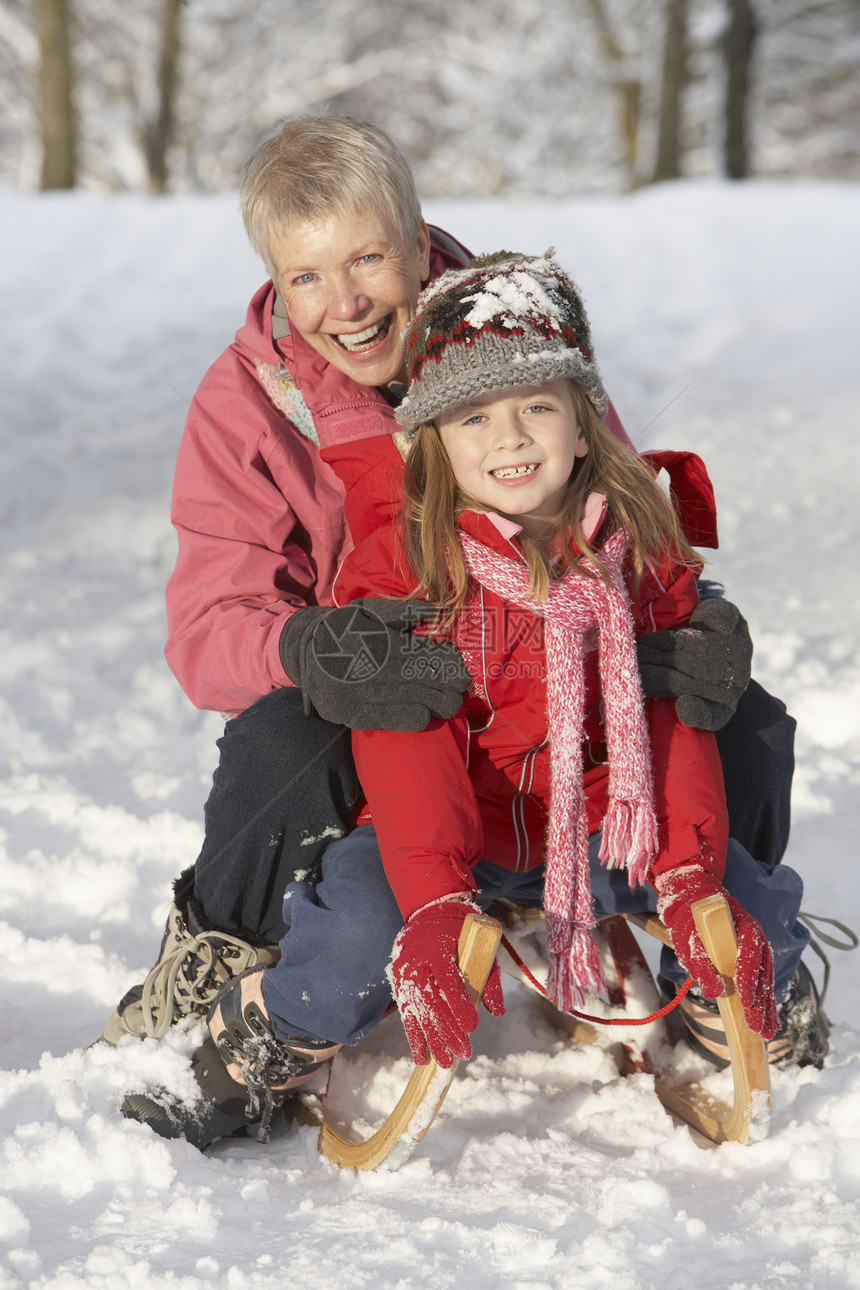 年青女孩与祖母在雪地风景中的滑雪上骑车公园林地微笑老年人笑声女性雪橇针织品天气两个人图片