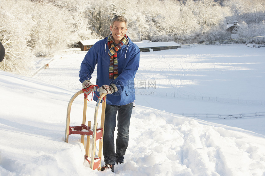 中年男子站在雪地景观控股悬崖水平场景下雪雪橇围巾微笑天气季节场地针织品图片