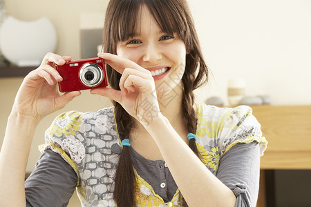 女青年在家里数码相机上拍摄摄影照片相机客厅长度爱好成人娱乐闲暇女性微笑水平背景图片