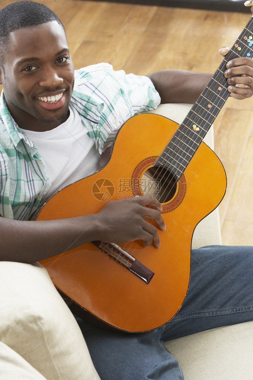 年轻人在索法玩音乐吉他时坐在沙发上微笑学习高架男性客厅练习乐器成人原声长度图片