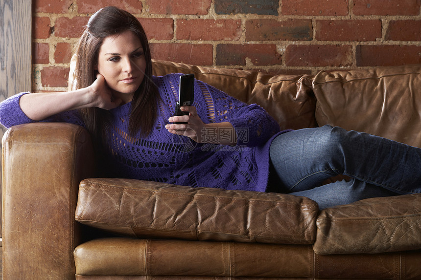 在沙发上打电话的年轻女青年牛仔裤长椅阅读皮革针织品沉思享受喜悦休息女性图片