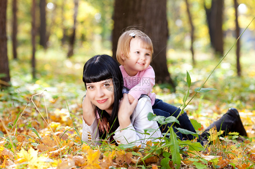 美丽的年轻母亲和女儿 躺在秋天的河里父母橙子喜悦孩子公园快乐叶子女士乐趣女孩图片