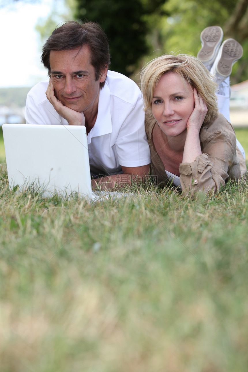 夫妇用笔记本电脑躺在草地上图片
